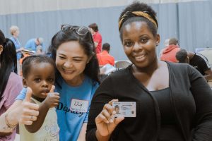 A mother and her daughter show of Mom's new ID with an IDignity volunteer from IBERIABANK